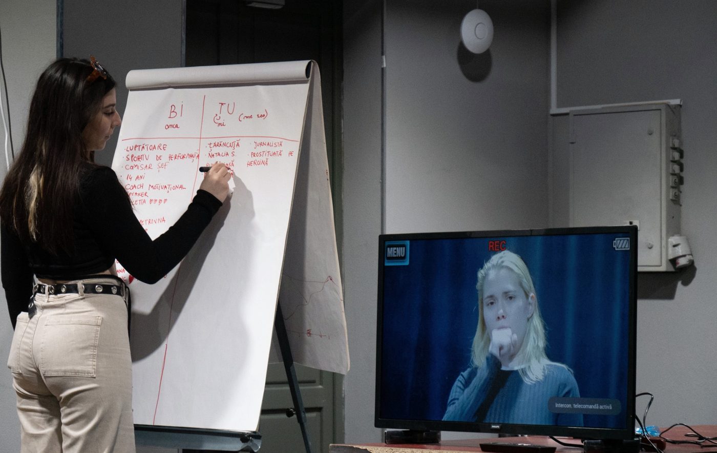 Cursantă lucrând la flipchart lângă ecranul cu înregistrarea, la masterclass